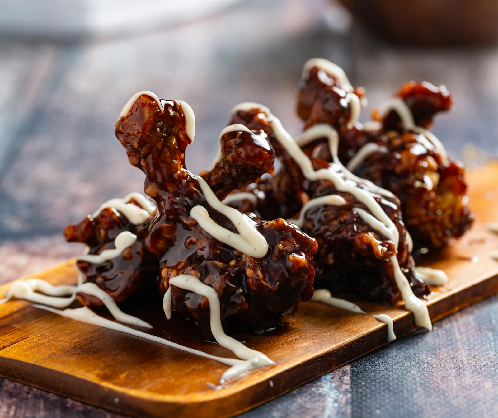Chicken thigh in house glaze with white-sauce drizzle on a wooden board