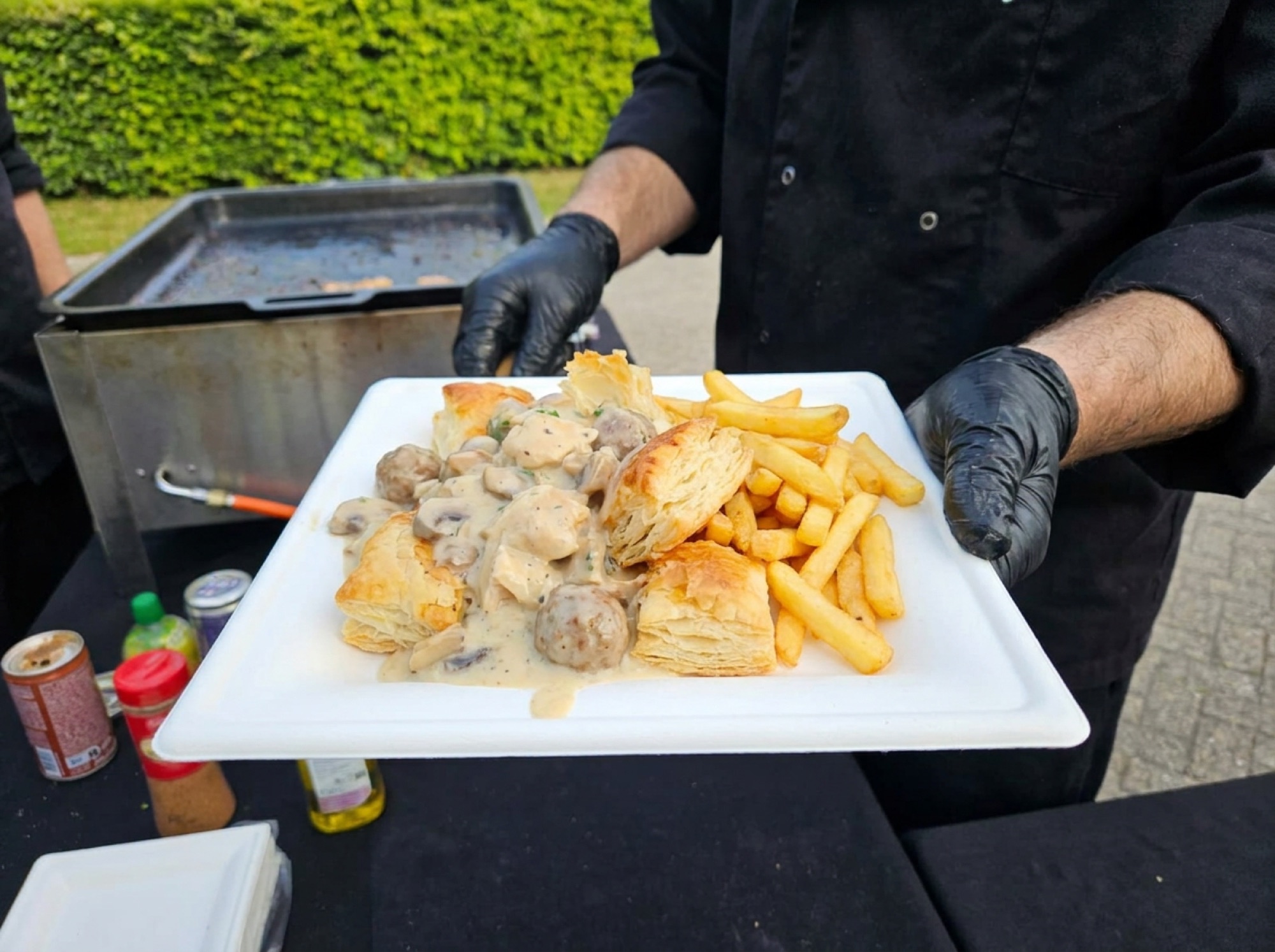Vol-au-vent met frieten op wit suikerrietbord, geserveerd met zwarte handschoenen