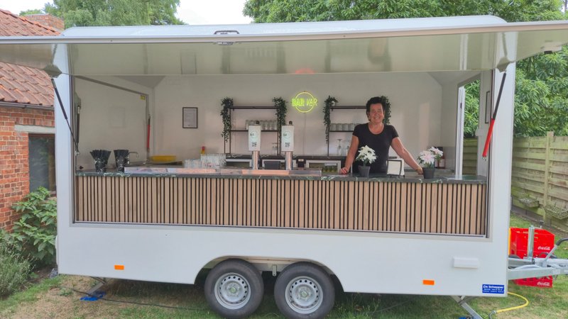 Nadine achter de Bar-Kaar trailer tijdens een avondevent, glas in de hand